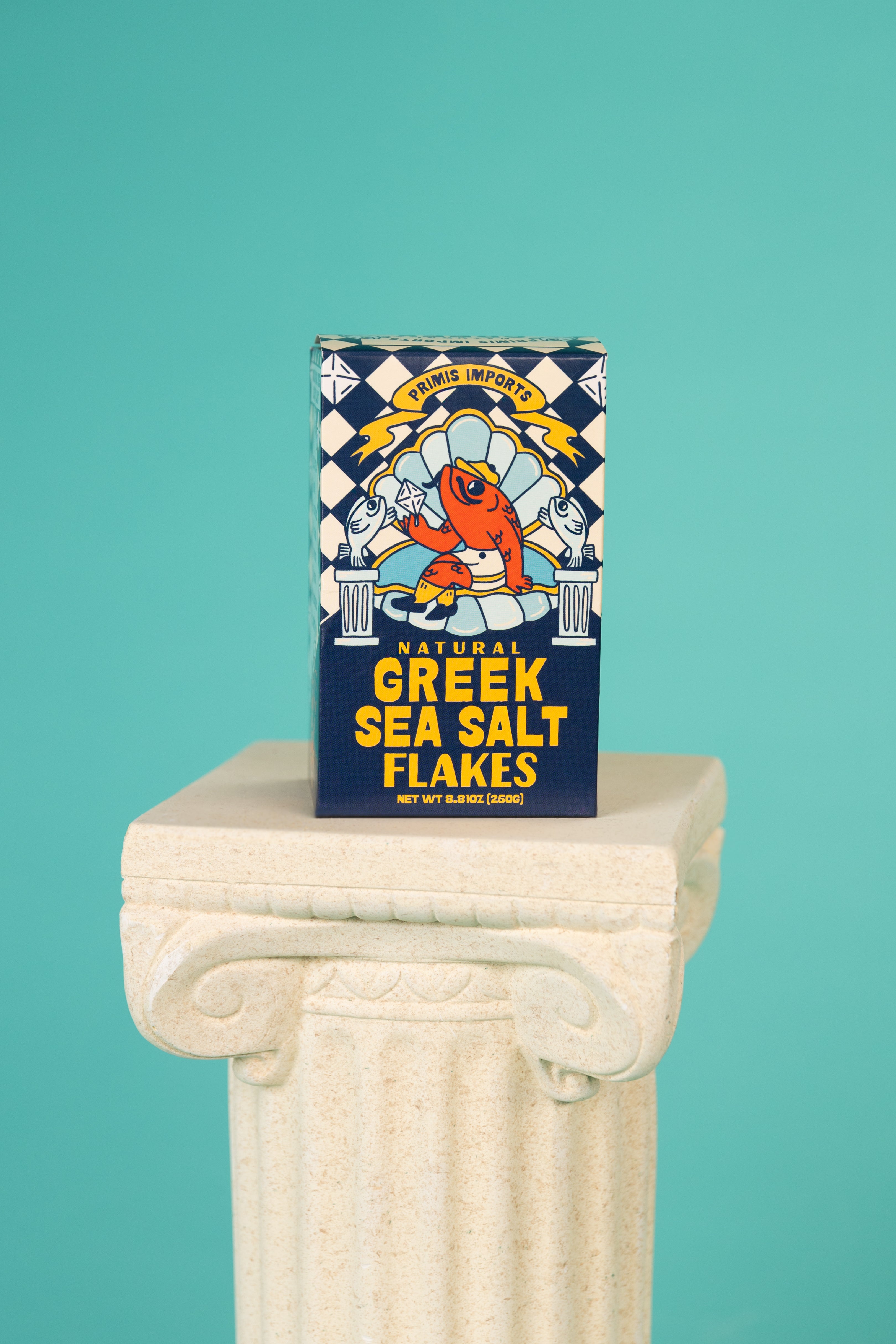 Box of Natural Greek Sea Salt Flakes on a decorative column against a teal background